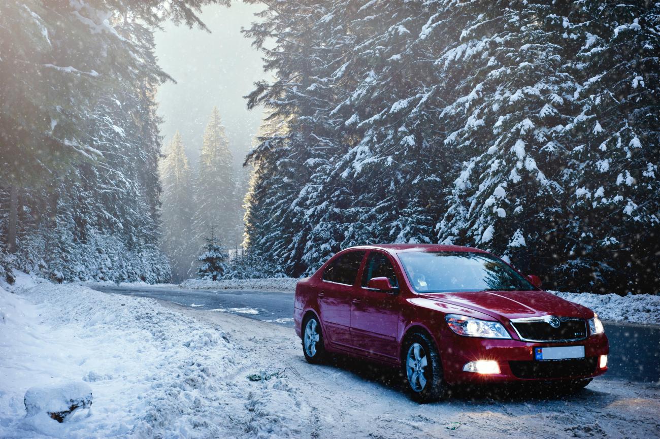 Red car parked on snowy road in forest